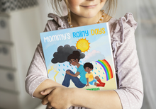 Load image into Gallery viewer, Child holding a book titled 'Mommy's Rainy Days' with a colorful cover featuring a mother and child under a rainbow.